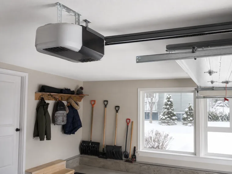 Ceiling-mounted garage door opener in a Marquette garage, snow shovels by the wall and a snowy yard through the window